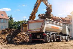 Heavy excavatore machine uploading waste and debris rubble into dump truck at construction site. Building dismantling and construction waste disposal service. Construction site industrial background