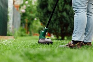 Man mows tall grass with an electric trimmer. Yard care concept